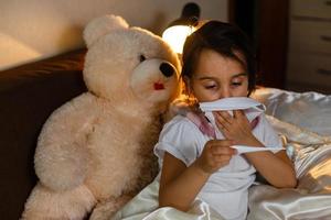 retrato en ángulo alto de una linda niña que sufre de frío mientras se acuesta en la cama foto