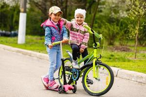 Happy girl friend ride roller skates scooter and bicycle on tow laughing happily photo