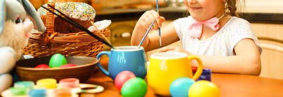 Happy easter A beautiful child girl painting Easter eggs. Happy family preparing for Easter. Cute little child girl wearing bunny ears on Easter day. photo