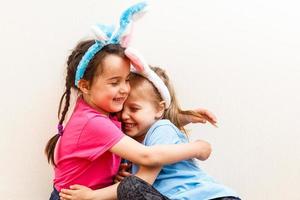 Two smiling girls with rabbit ears holding a box with easter eggs on background. photo