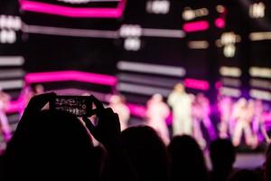 un teléfono inteligente sostenido con dos manos para filmar un metraje durante un concierto. foto