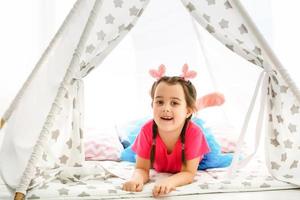 A little girl sits in a wigwam with pillows photo