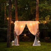 decoración de la ceremonia del crepúsculo de la boda hecha de linternas y lámparas doradas colgadas en un árbol y velas encendidas sobre la hierba con la alfombra en el medio foto