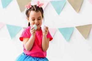 Getting ready to Easter. Lovely little girl holding an Easter egg and smiling with decoration in the background photo