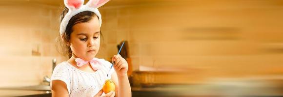 una linda niña pequeña con orejas de conejo se sienta en el suelo con una canasta de huevos de Pascua. foto