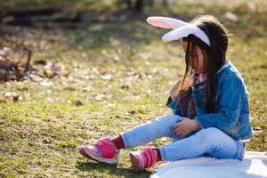 Unhappy little sad bunny girl sits alone in the spring garden. Easter time photo