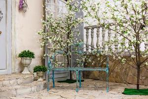 Spring patio of blue wooden house with blooming oriental cherry on a terrace white bench with photo