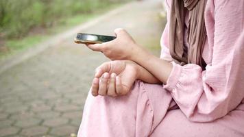 junge muslimische Frau mit Smartphone, während sie auf einer Parkbank sitzt video