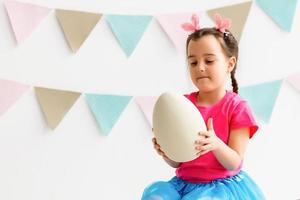 Getting ready to Easter. Lovely little girl holding an Easter egg and smiling with decoration in the background photo