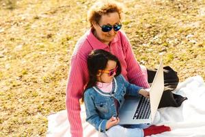 Modern grandmother teaching grandchild how to use laptop computer photo