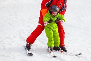 Little girl in red learning to ski with the help of an adult photo