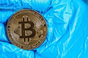 Hand with blue, medical gloves holding a golden bitcoin photo