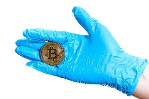 Hand with blue, medical gloves holding a golden bitcoin photo