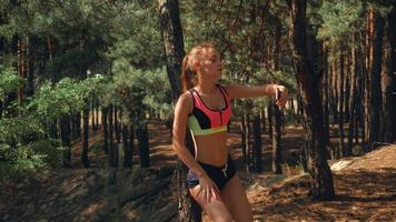 atletisch mooi meisje in kort shorts en top staat in de buurt een boom en maakt een foto Aan uw telefoon video