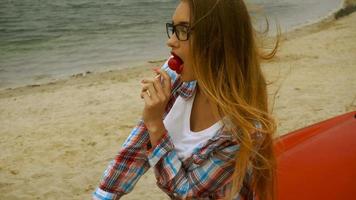 beautiful blonde lady with red lips licks a lollipop on a seashore video