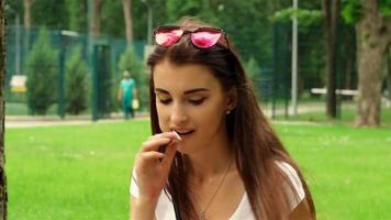 alla moda giovane ragazza nel bicchieri su sua testa si siede nel il parco e fa schifo lecca-lecca video