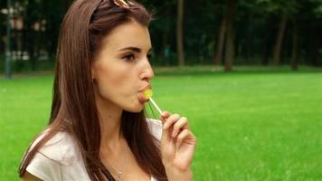 beautiful young girl licks lollipop in Park close up video