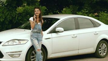 menina bonita sorridente em pé perto do carro e disse pelo celular video