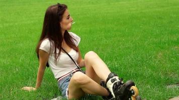 young cute girl with candy in mouth sitting on the grass in rollers video