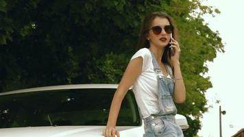 charming young lady beside her car says on a cell phone and smiling video