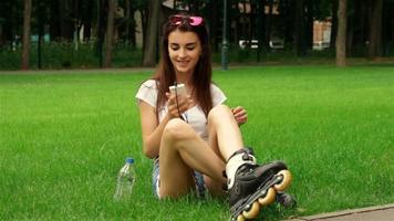 beautiful young lady listens to music with headphones and sitting on the grass in rollers video