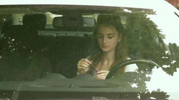jong aantrekkingskracht meisje zit in de auto looks in de spiegel en verf lippen video