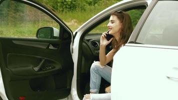 bonne belle fille assise dans la voiture avec la porte ouverte et parlant au téléphone video