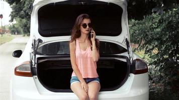 young elegant Lady in the mirrored glasses stands near the white car and speaks on a mobile telephone video