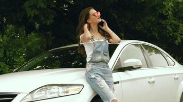 fashionable young brunette in glasses speaks on a mobile telephone near her car on the street video