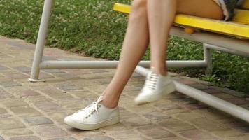 young girl in white sneakers is sitting on a swing close up video