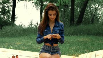 jeune fille en chemise est assise dans la rue et tient un téléphone en gros plan video