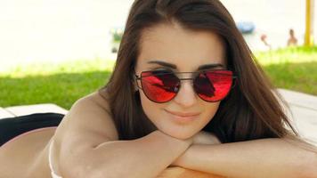 una joven atractiva con gafas de espejo yacía en la playa, de cerca video