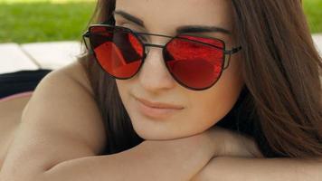 bella morena sonriente con gafas en la playa tomando el sol de cerca video