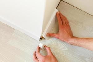 Hands fitting the baseboard to a bright wall photo