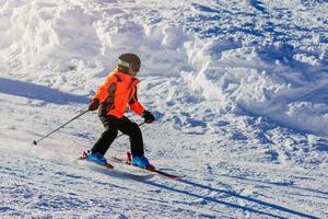 The boy in a green jacket on skis in mountains photo