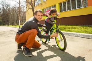 Happy father teaching his little daughter to ride a bicycle. Child learning to ride a bike. Family activities at summer. photo