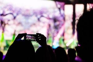 un teléfono inteligente sostenido con dos manos para filmar un metraje durante un concierto. foto