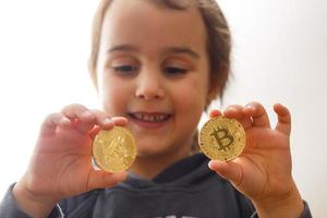 niña sonriente sosteniendo dos bitcoins de oro en sus manos pensando en moneda criptográfica foto