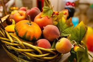 cesta con melocotones y peras calabaza amarilla madura entre hojas de otoño en un alféizar foto