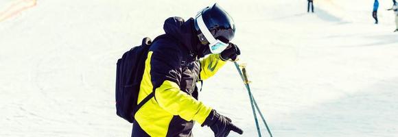 Skier holding ski and looking at beautiful snow covered mountains. Young man thinking and looking snowy mountain with copy space. Side view of winter skier guy with mask holding ski equipment outdoor. photo