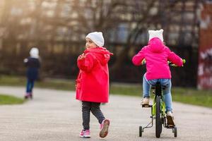 Little girl is riding a bicycle. another girl is runiinig alongside photo