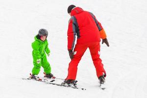 little girl learns to ski with the help of an adult photo