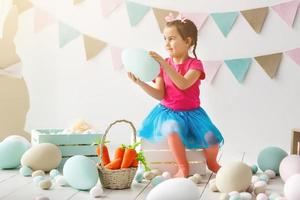 Getting ready to Easter. Lovely little girl holding an Easter egg and smiling with decoration in the background photo