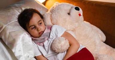 Sick girl with a thermometer in mouth lying in bed grumpy face photo