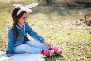 Adorable little girl wearing bunny ears on Easter day. Girl sitting on a green grass photo