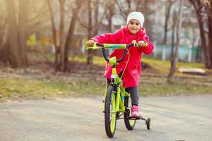 Little girl in red riding a bicycle outdoors photo