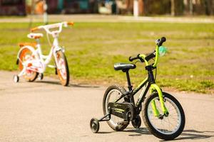 una bicicleta infantil baja de dos ruedas, blanca y morada, con ruedas laterales adicionales, se encuentra en medio del parque y vive su pequeño dueño. foto