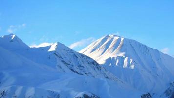 tiro estático de lapso de tempo de nuvens voadoras sobre os picos nevados das montanhas kazbegi cáucaso durante o dia ensolarado e o céu azul claro video