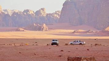 Wadi rum desert landscape with tourist trekking and line of 4wd vehicles drive on valley desert sandy road on organized safari tour in Jordan video