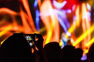 un teléfono inteligente sostenido con dos manos para filmar un metraje durante un concierto. foto